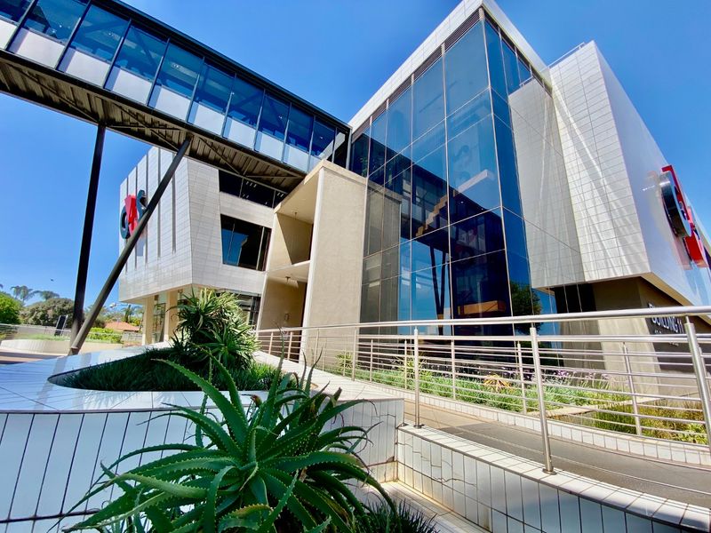 Modern commercial building exterior featuring a glass curtain wall, elevated pedestrian bridge, and tiled facade with ramp access.