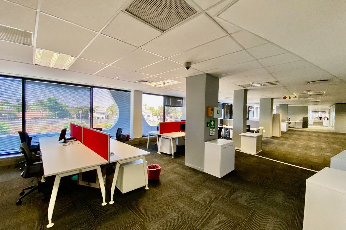 Open-plan commercial office space featuring carpeted flooring, suspended ceilings with recessed lighting, large windows, and integrated air conditioning.
