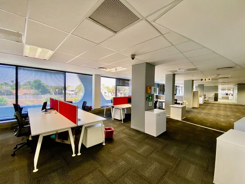 Open-plan commercial office space featuring carpeted flooring, suspended ceilings with recessed lighting, large windows, and integrated air conditioning.