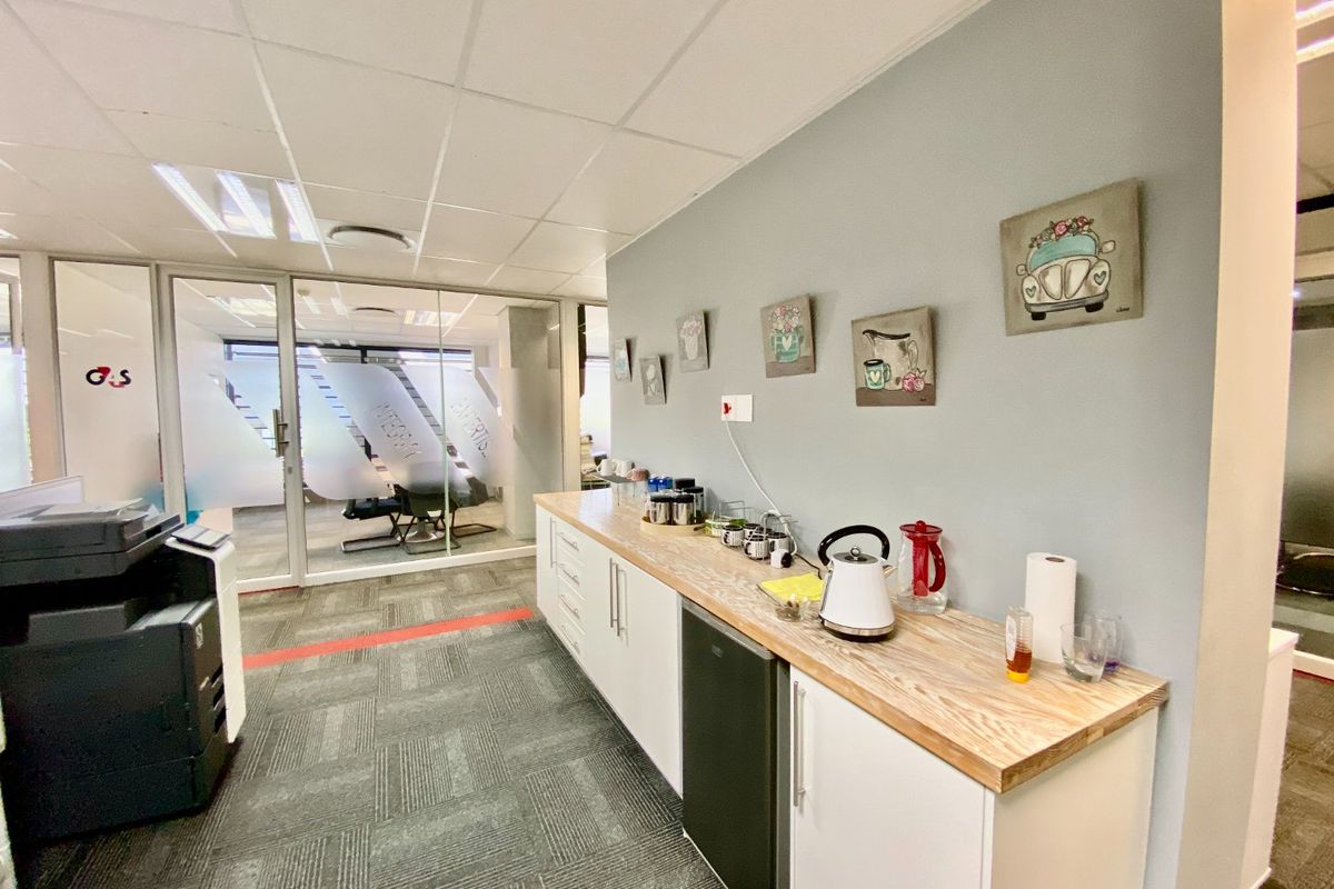 A functional office kitchenette featuring built-in cabinetry, a wood-look countertop, and a glass partition wall, providing a clean and professional break area.