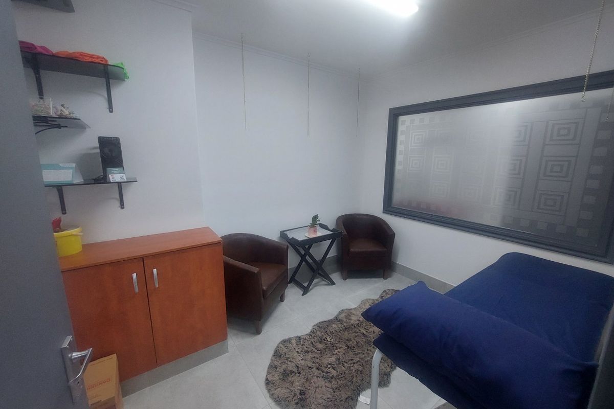 A functional office or treatment room featuring tiled flooring, built-in cabinetry, wall-mounted shelving, and a large frosted glass window.
