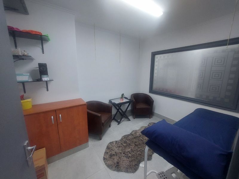 A functional office or treatment room featuring tiled flooring, built-in cabinetry, wall-mounted shelving, and a large frosted glass window.