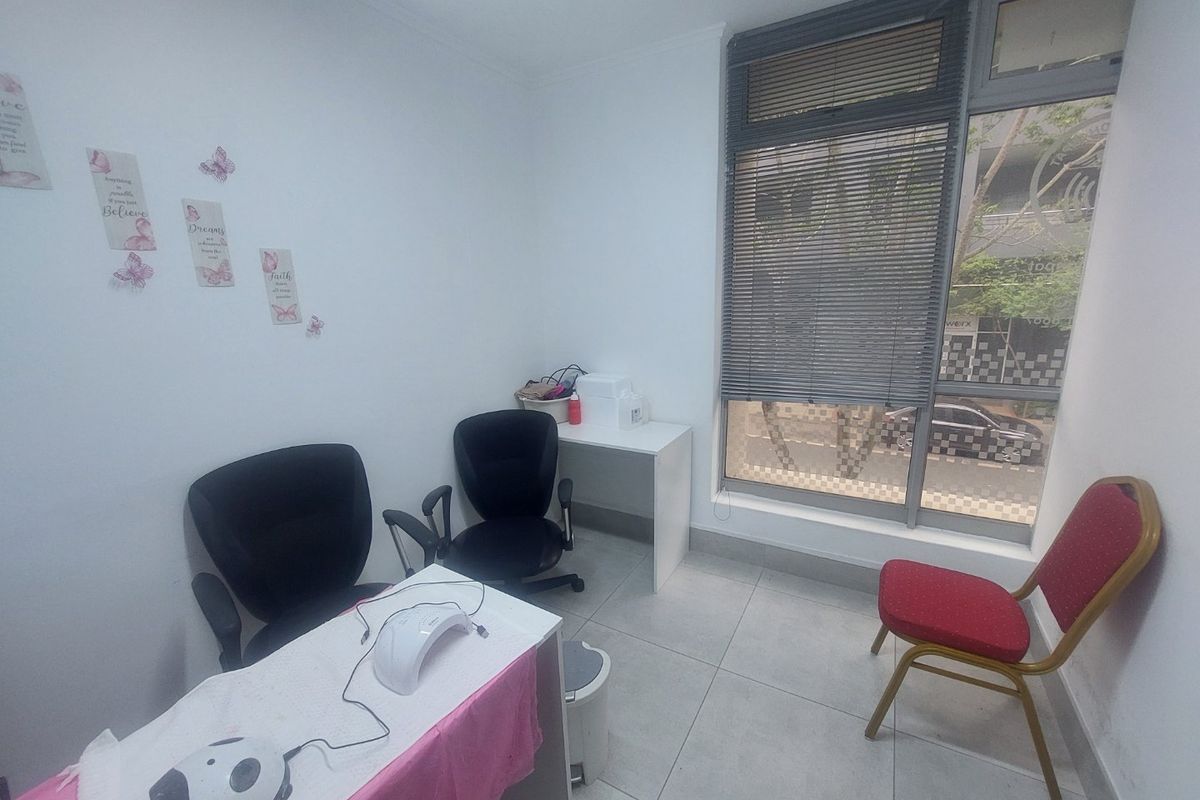 A compact commercial office space featuring large windows with venetian blinds and neutral tiled flooring, suitable for a small consultation or service room.