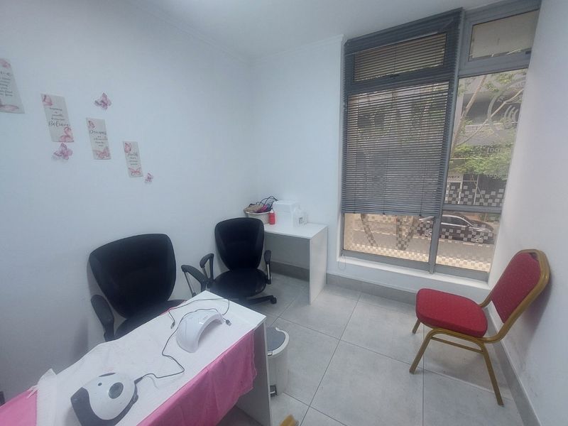 A compact commercial office space featuring large windows with venetian blinds and neutral tiled flooring, suitable for a small consultation or service room.
