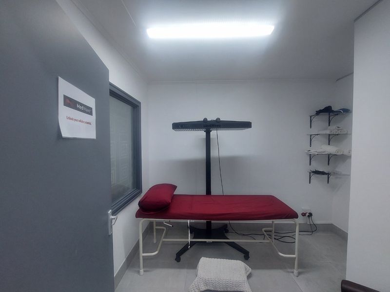 A functional clinical treatment room featuring tiled flooring, wall-mounted shelving, and overhead fluorescent lighting, suitable for medical or wellness services.