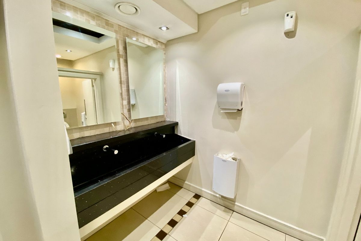 A clean commercial bathroom featuring a long built-in vanity with dual mirrors, recessed lighting, and tiled flooring.