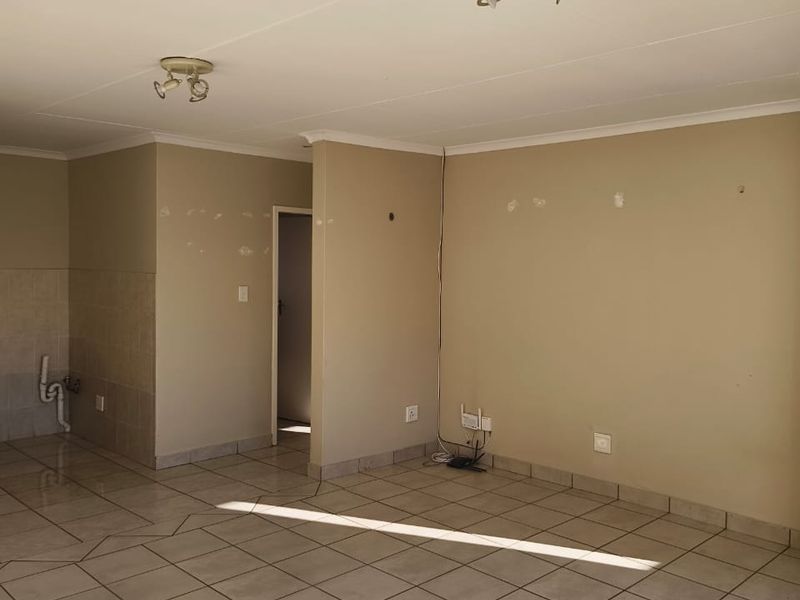 An empty open-plan living area featuring ceramic floor tiles, ceiling lighting, and visible wall surface imperfections requiring minor repair.