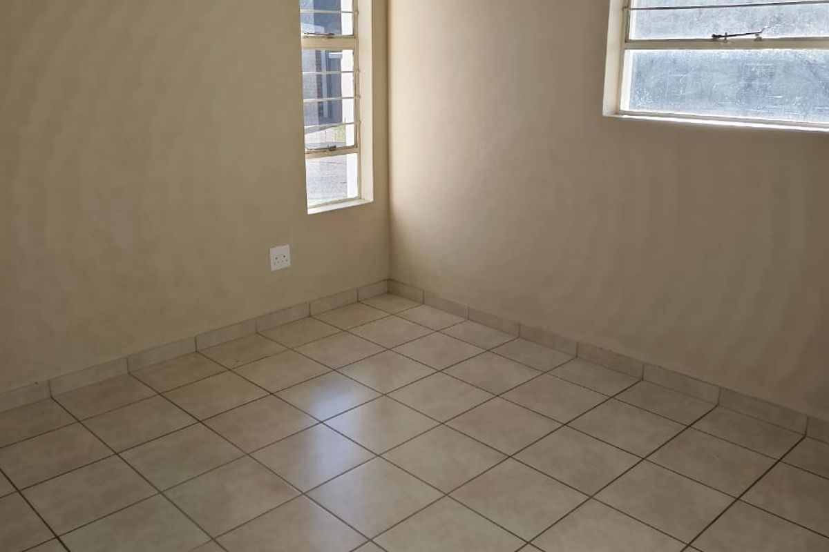 An empty bedroom featuring neutral tiled flooring, large windows with security bars, and coved ceilings, offering a blank canvas for personalization.