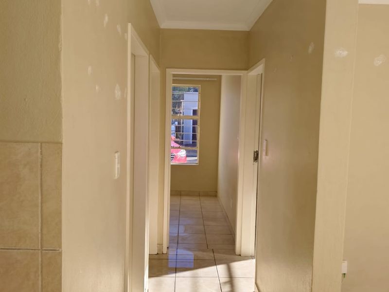 A vacant hallway featuring tiled flooring and recessed lighting, currently requiring minor wall repairs and a fresh coat of paint.
