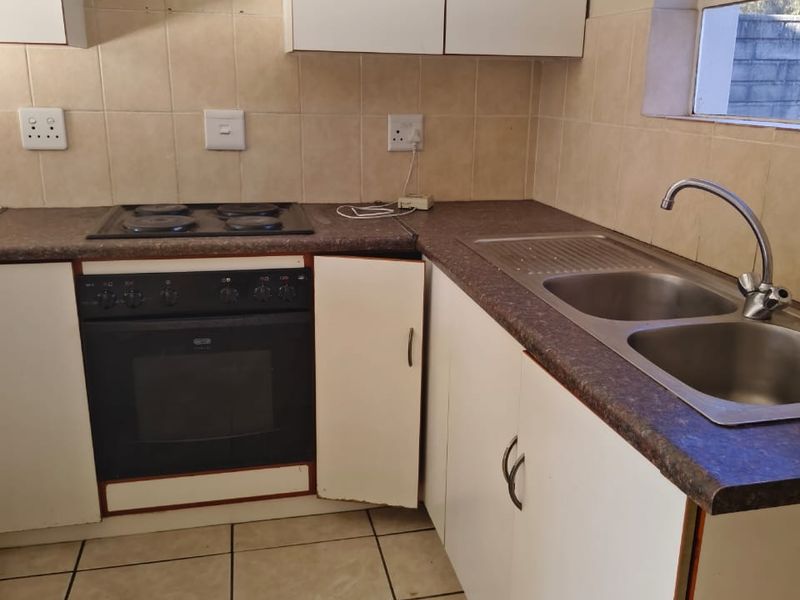 A functional kitchen featuring built-in cabinetry, an electric oven and hob, double sink, and tiled finishes, requiring minor cosmetic updates.