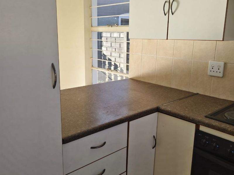 A compact kitchen featuring built-in cabinetry, a laminate countertop, tiled backsplash, and an integrated oven and hob, offering a functional layout for renovation.