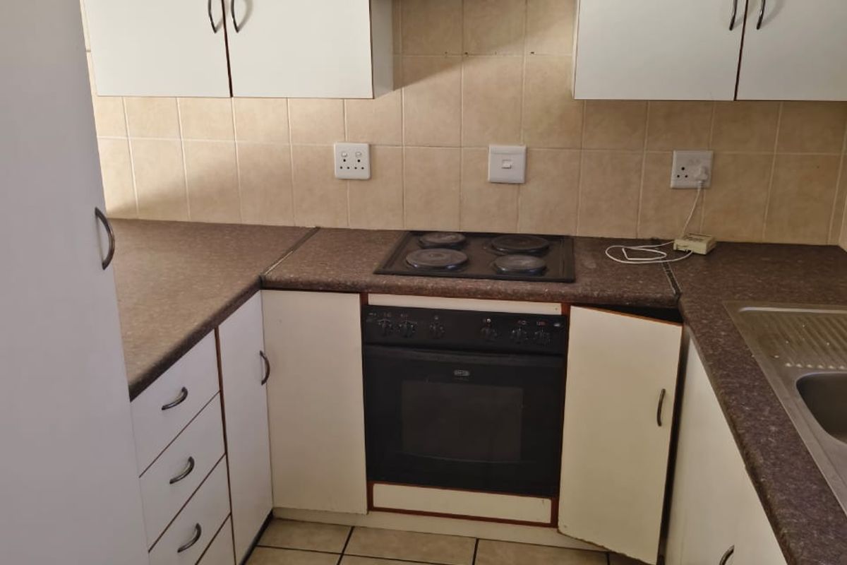 A compact kitchen featuring white cabinetry, laminate countertops, a built-in oven and hob, and tiled finishes, requiring minor repairs to cabinetry.