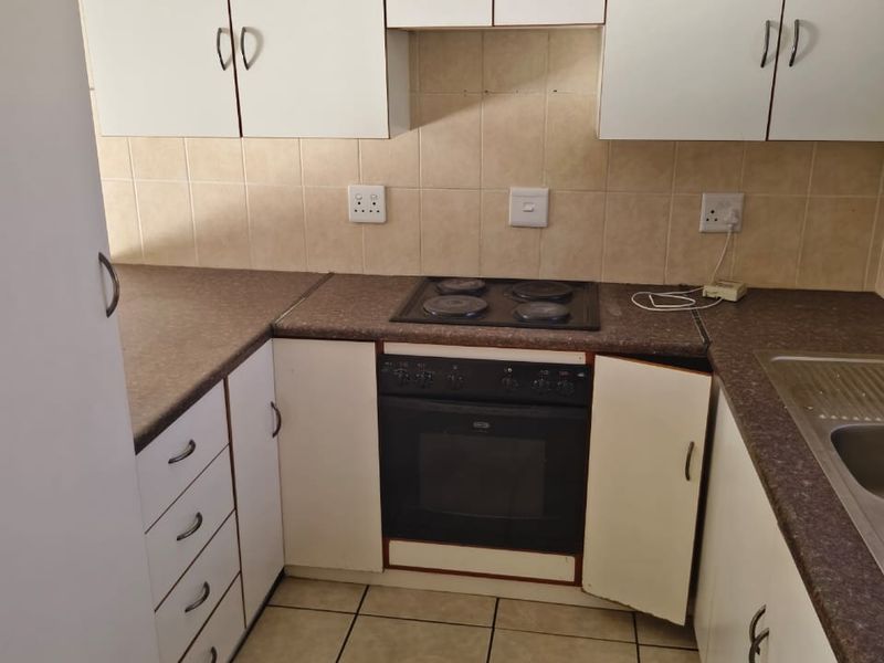 A compact kitchen featuring white cabinetry, laminate countertops, a built-in oven and hob, and tiled finishes, requiring minor repairs to cabinetry.