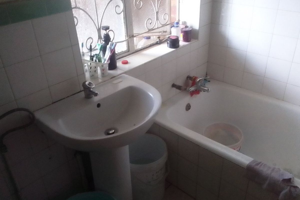 A functional bathroom featuring a pedestal basin, bathtub, and tiled walls, currently requiring maintenance and cosmetic updates to improve its overall condition.