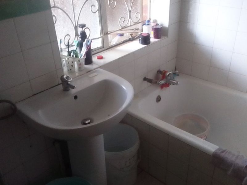 A functional bathroom featuring a pedestal basin, bathtub, and tiled walls, currently requiring maintenance and cosmetic updates to improve its overall condition.