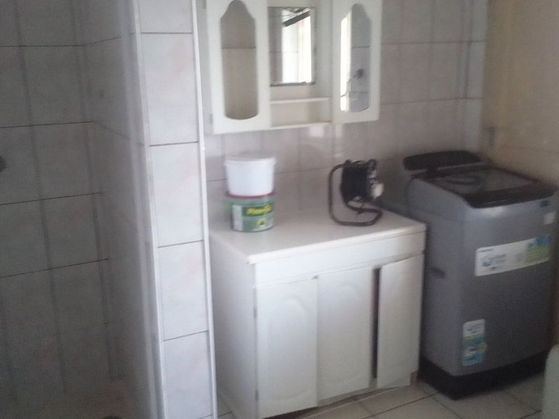A functional laundry area featuring tiled walls, a built-in vanity cabinet, and an adjacent shower enclosure, offering potential for modernization.