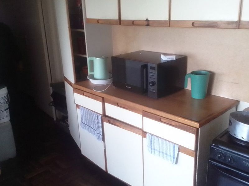 A dated kitchen area featuring original cabinetry, laminate countertops, and a freestanding stove, offering potential for a modern renovation.