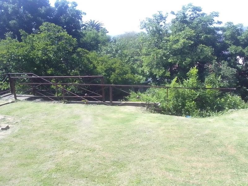 A sloped garden area featuring a lawn, stone edging, and a metal safety railing overlooking mature trees.
