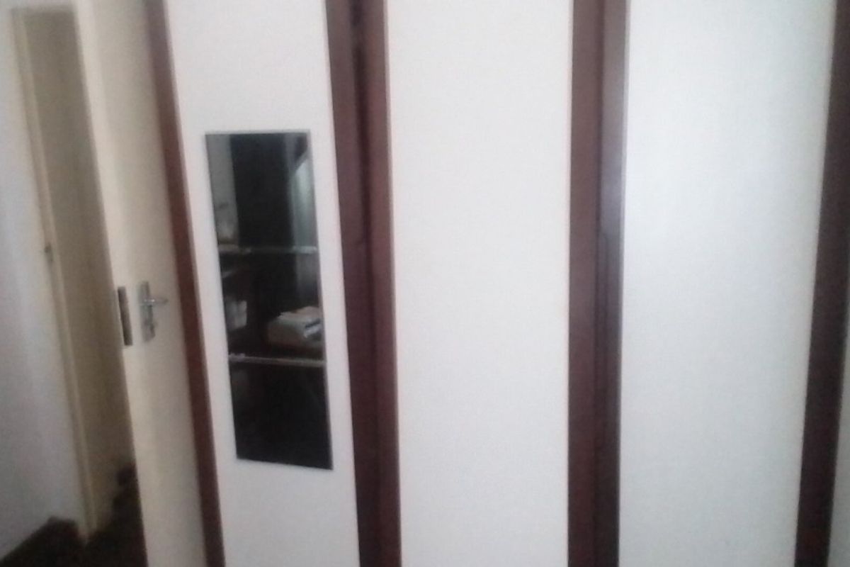 A bedroom interior featuring built-in cupboards with dark wood trim and a small integrated mirror panel.