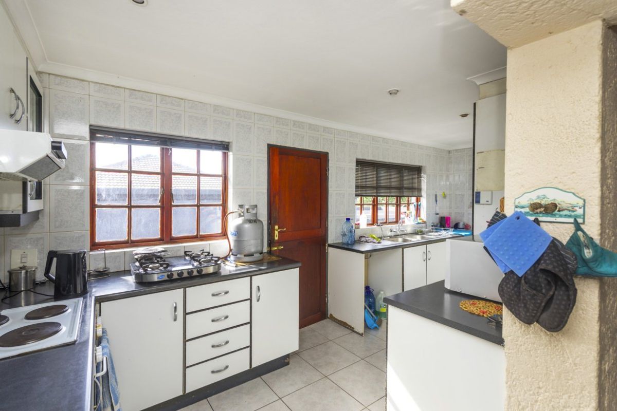 A functional kitchen featuring a gas and electric hob, double sink, tiled splashbacks, and ample built-in cabinetry with laminate countertops.