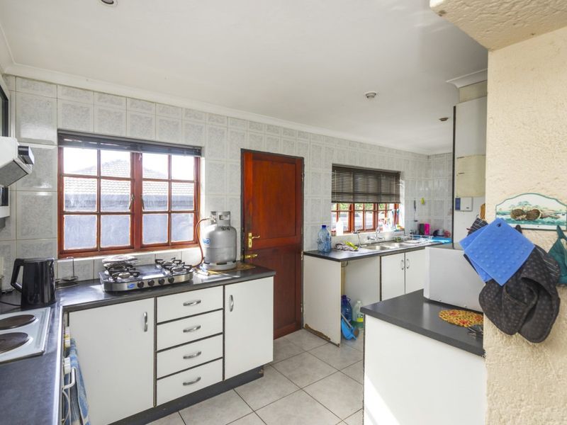 A functional kitchen featuring a gas and electric hob, double sink, tiled splashbacks, and ample built-in cabinetry with laminate countertops.