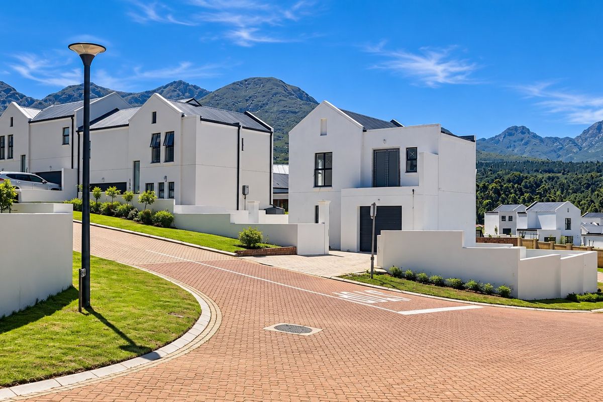 A view of a modern residential street featuring white contemporary homes, paved driveways, and well-maintained landscaping against a scenic mountain backdrop.
