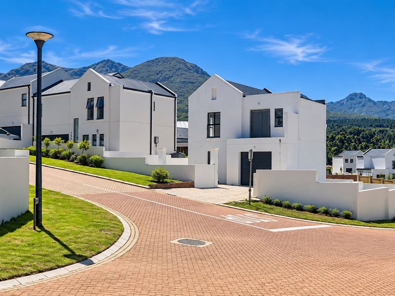 A view of a modern residential street featuring white contemporary homes, paved driveways, and well-maintained landscaping against a scenic mountain backdrop.