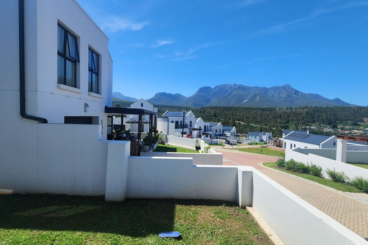 A view of the rear exterior of the property featuring a paved driveway, boundary walls, and scenic mountain views in the background.