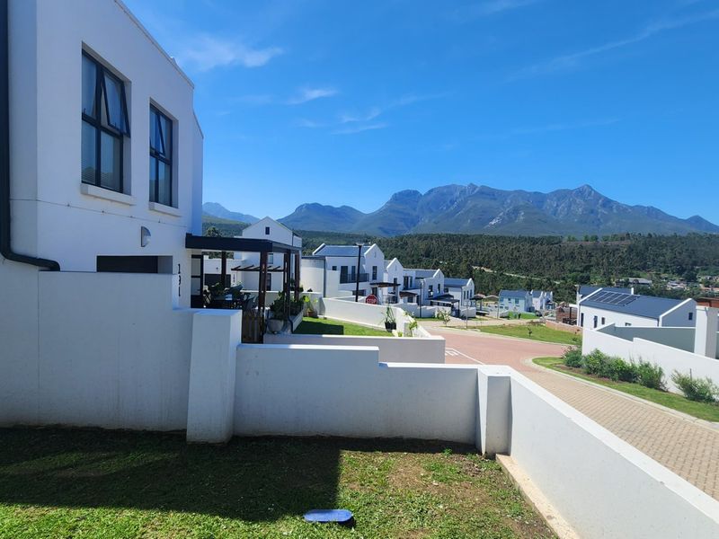A view of the rear exterior of the property featuring a paved driveway, boundary walls, and scenic mountain views in the background.