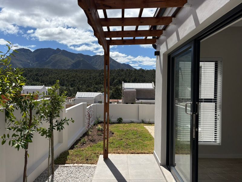 A modern patio featuring a wooden pergola, tiled flooring, and a sliding glass door, overlooking a landscaped garden with scenic mountain views.