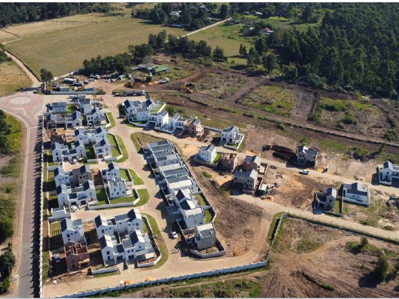 Aerial view of a residential housing development estate showing multiple completed and under-construction units with paved access roads and perimeter fencing.