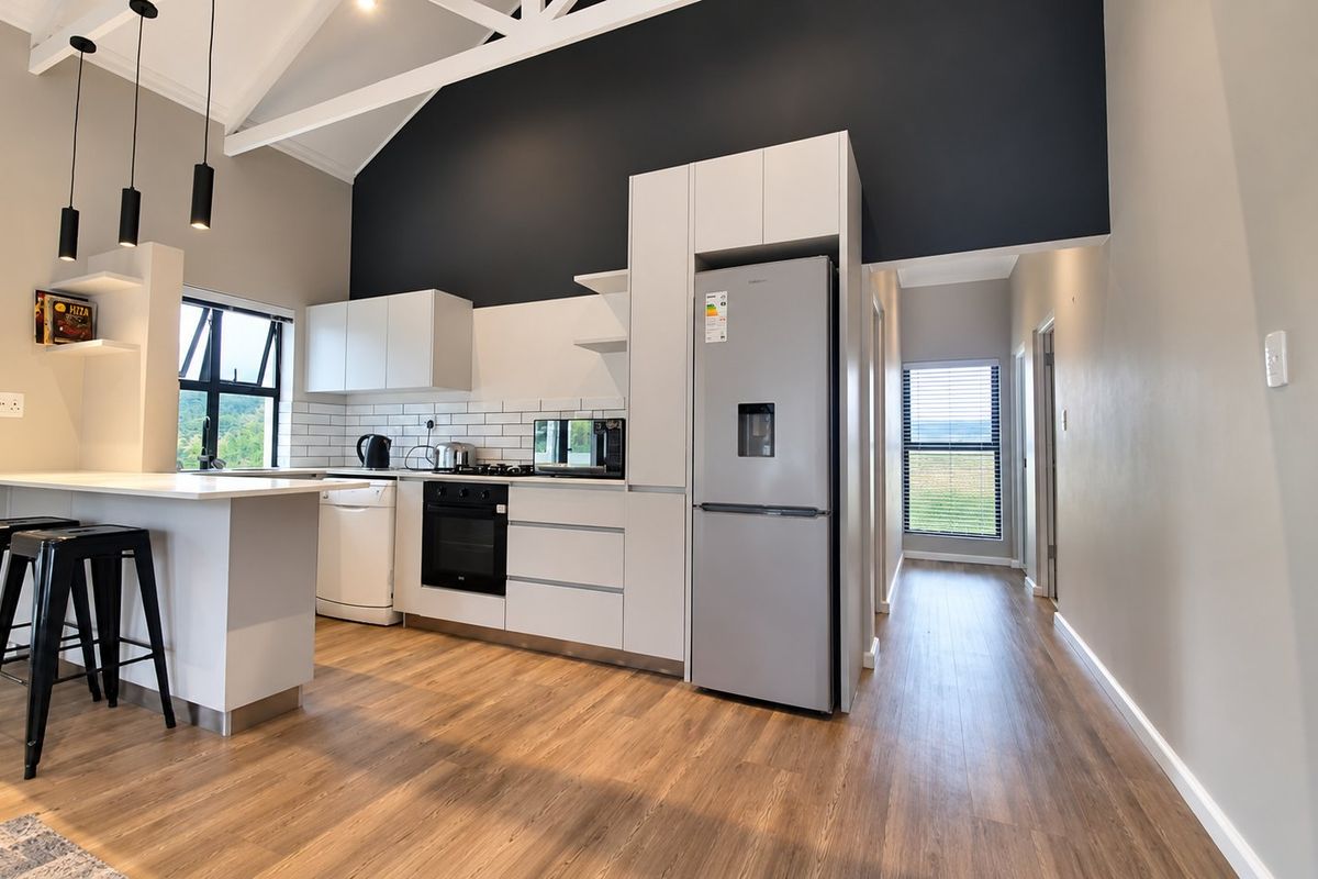 Modern kitchen featuring sleek white cabinetry, subway tile backsplash, built-in oven, and a breakfast bar under a high vaulted ceiling.