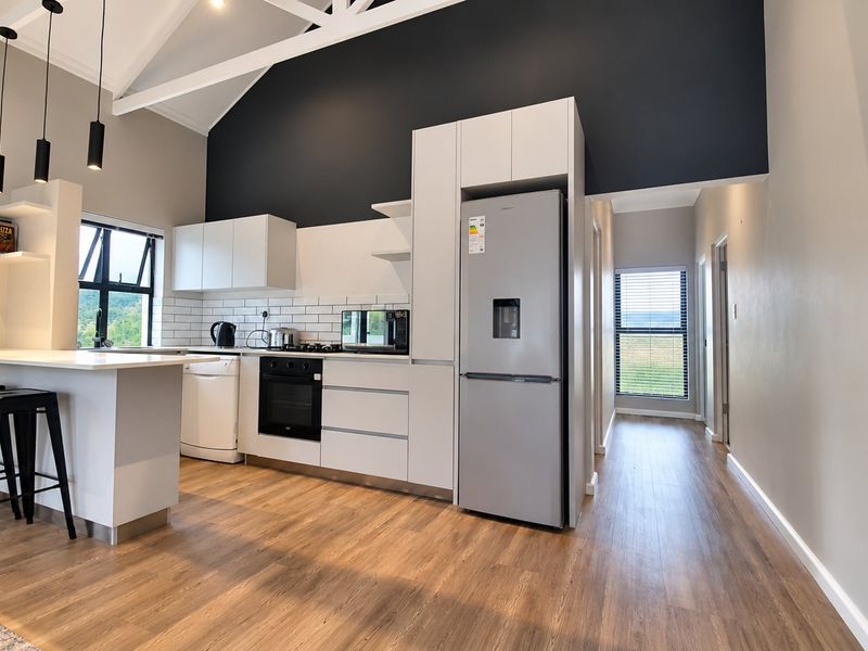 Modern kitchen featuring sleek white cabinetry, subway tile backsplash, built-in oven, and a breakfast bar under a high vaulted ceiling.