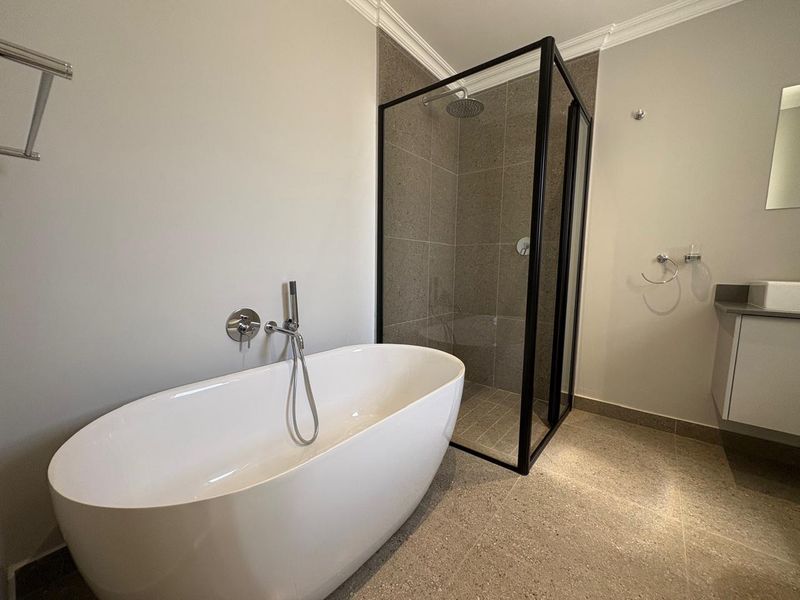 Modern bathroom featuring a sleek freestanding bathtub, a walk-in shower with a black frame, and a contemporary vanity unit.
