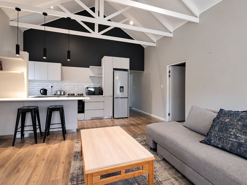 Modern open-plan living area featuring a contemporary kitchen with sleek cabinetry, subway tile backsplash, and a striking vaulted ceiling with exposed white trusses.