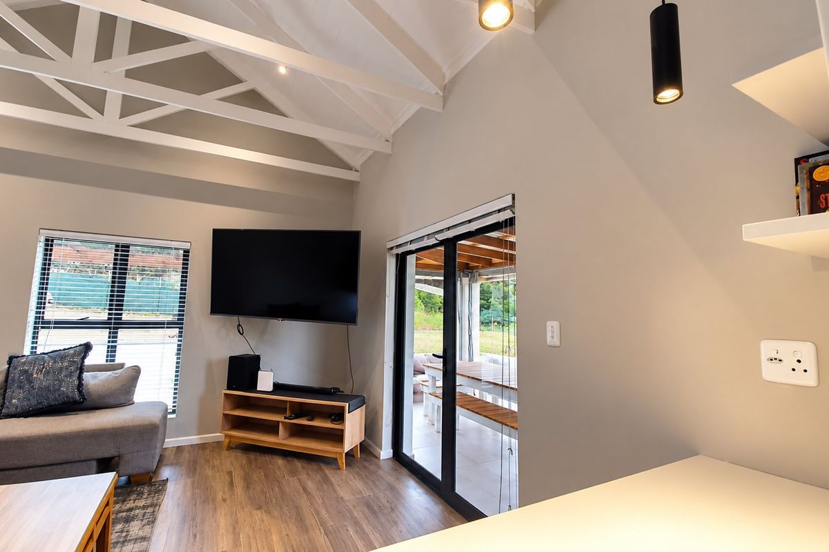 Bright living room featuring high vaulted ceilings with exposed trusses, laminate flooring, and large sliding doors providing seamless access to the outdoor patio area.