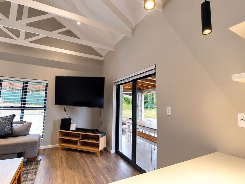 Bright living room featuring high vaulted ceilings with exposed trusses, laminate flooring, and large sliding doors providing seamless access to the outdoor patio area.