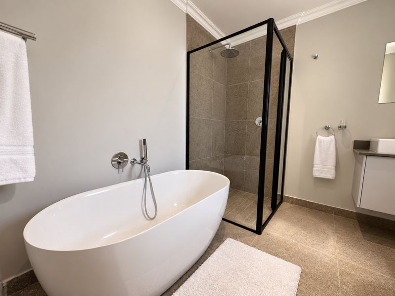 Modern bathroom featuring a sleek freestanding bathtub, a walk-in shower with a black frame, and a contemporary vanity unit.