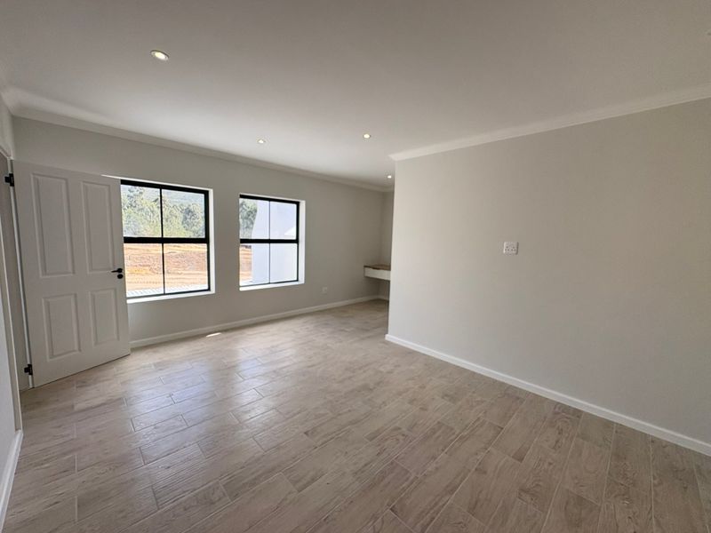 A bright, empty bedroom featuring modern tiled flooring, recessed downlights, and a built-in desk area, offering a clean and neutral canvas.