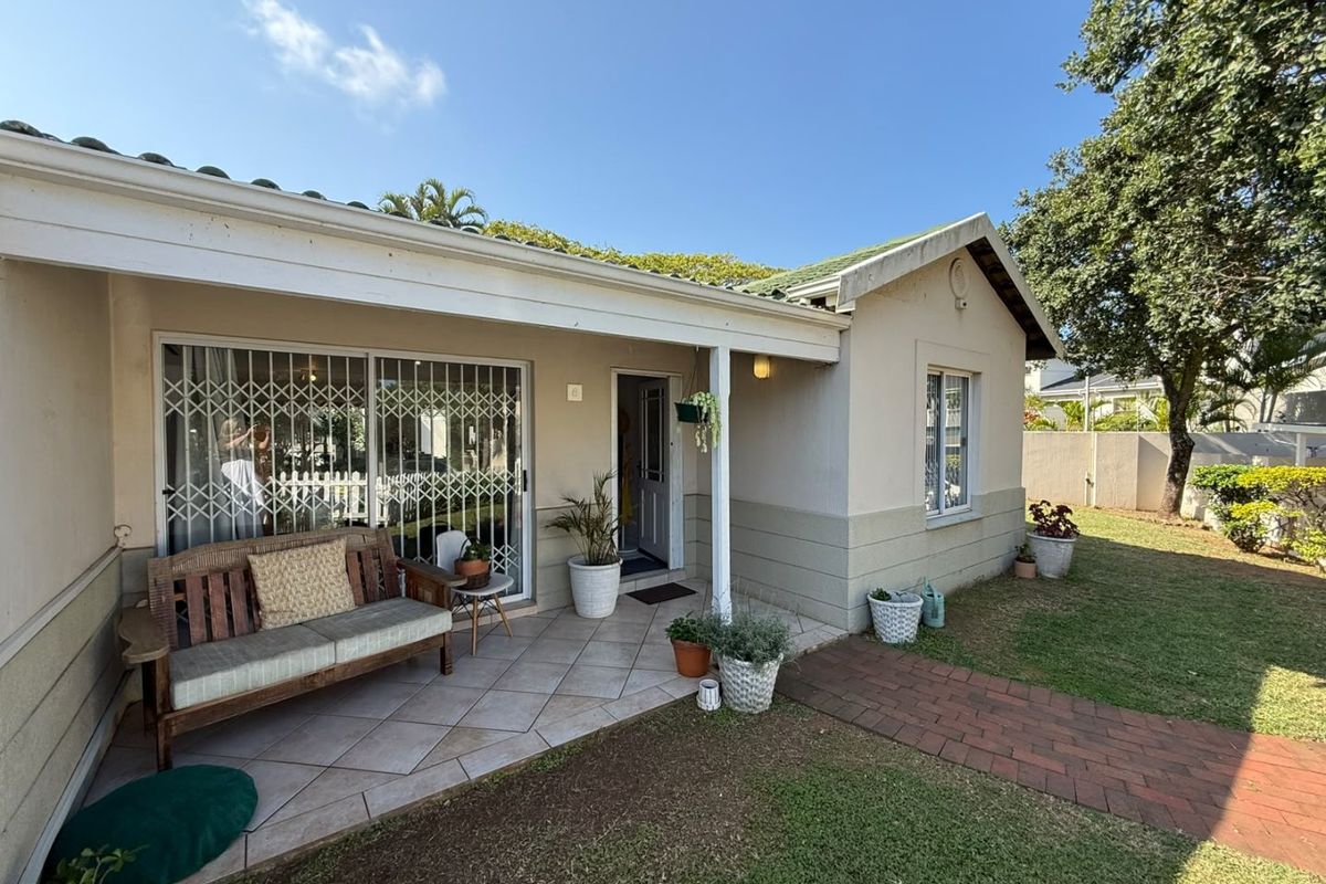 A well-maintained rear exterior view of the townhouse featuring a covered tiled patio, brick walkway, and established garden area.