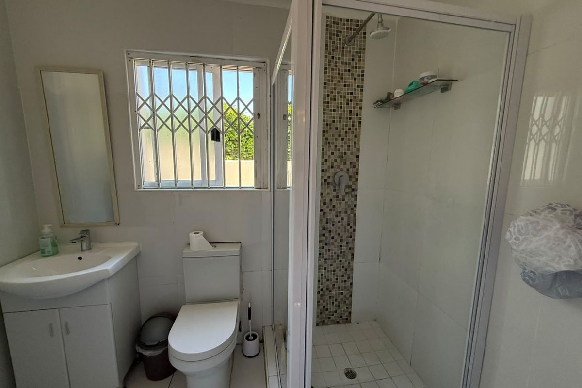 A functional bathroom featuring a vanity unit, toilet, and a glass-enclosed shower with a decorative mosaic tile accent wall.