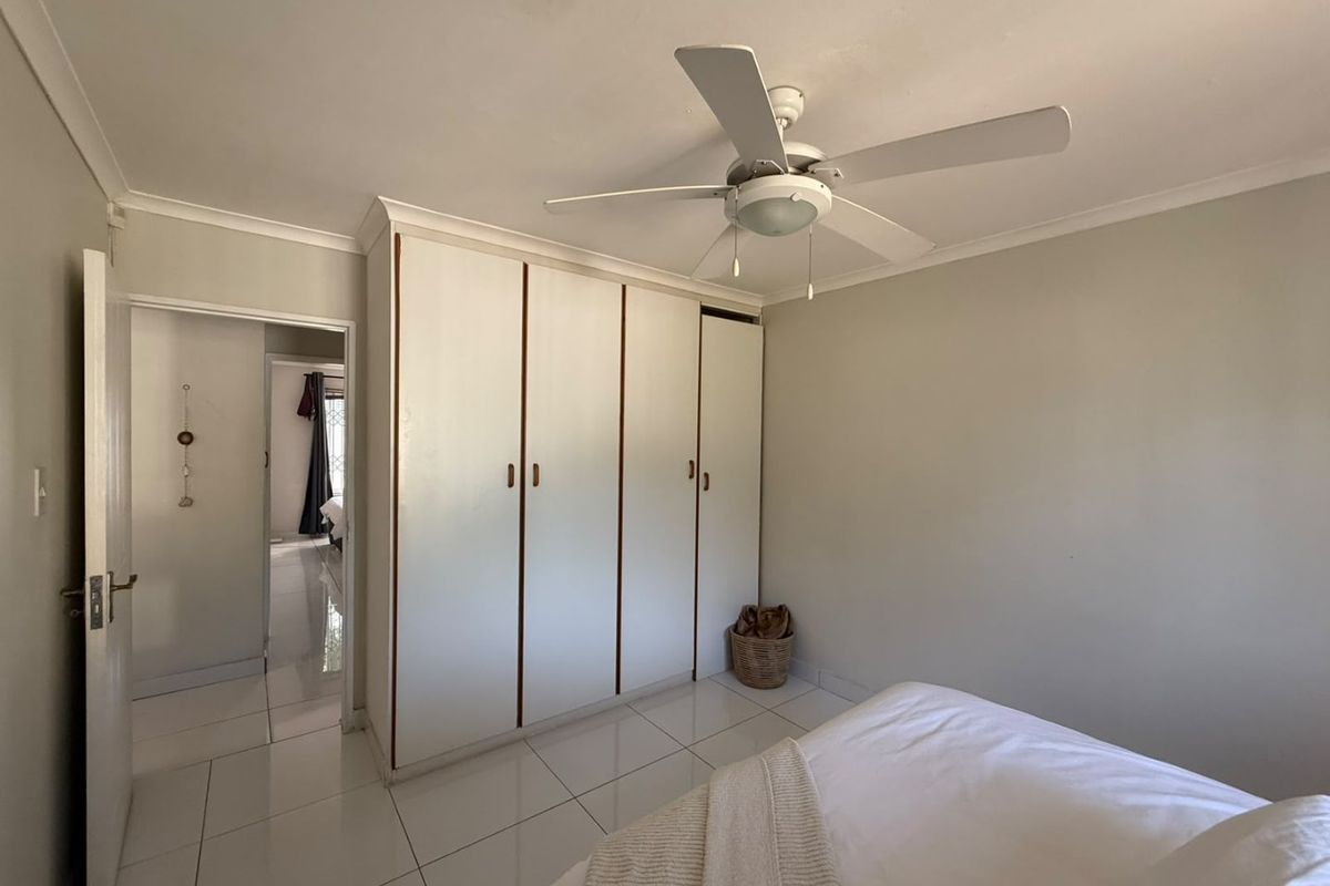 A bedroom featuring built-in cupboards, a ceiling fan, and tiled flooring, providing a functional and neutral living space.