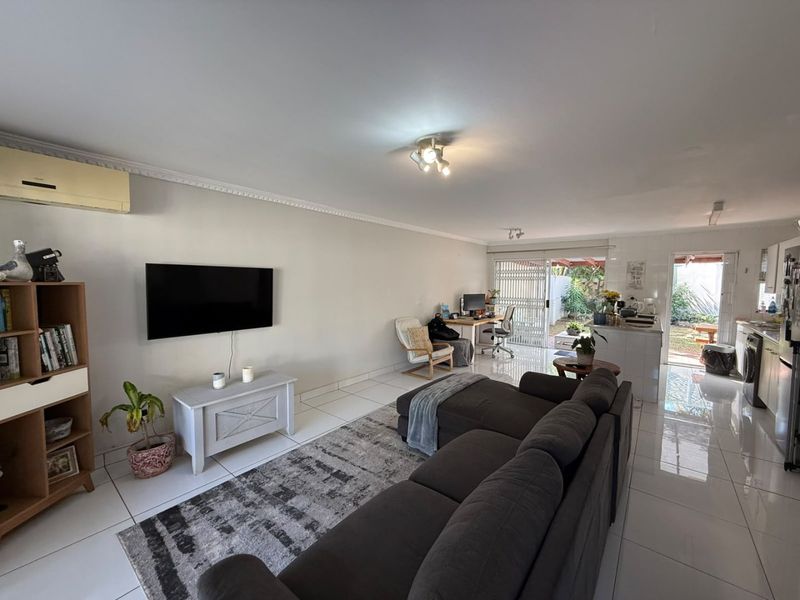 Spacious open-plan living and kitchen area featuring tiled flooring, split-system air conditioning, and direct access to the rear patio through sliding glass doors.