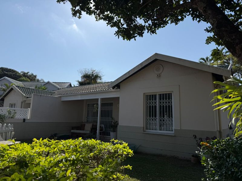 Rear view of the townhouse featuring a covered patio, tiled roof, and security bars on windows, set within a private garden area.