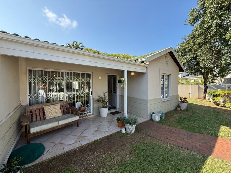A well-maintained rear exterior view of the townhouse featuring a covered tiled patio, brick walkway, and established garden area.