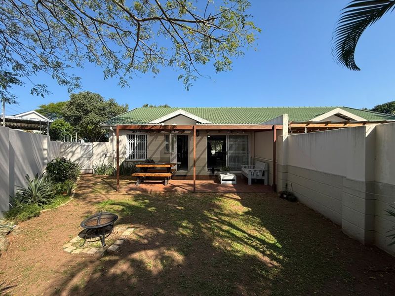 Rear view of the townhouse featuring a paved patio with a timber pergola, enclosed by boundary walls and a private garden area.