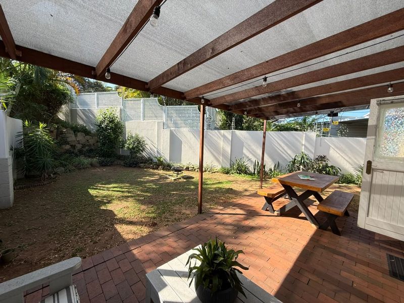 Covered outdoor patio area featuring a timber pergola with shade cloth, brick paving, and access to a private garden with perimeter fencing.
