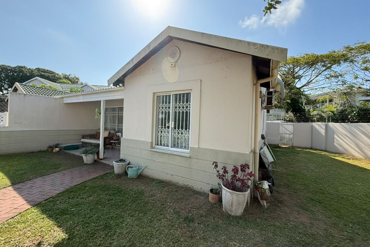 Rear view of the townhouse featuring a covered patio, brick paved walkway, and a private garden area enclosed by boundary walls with electric fencing.