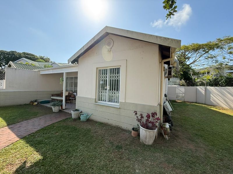 Rear view of the townhouse featuring a covered patio, brick paved walkway, and a private garden area enclosed by boundary walls with electric fencing.