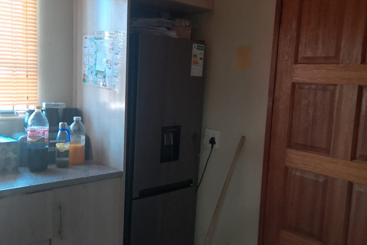 A functional kitchen area featuring built-in cabinetry, laminate countertops, and tiled flooring, adjacent to a traditional timber door.